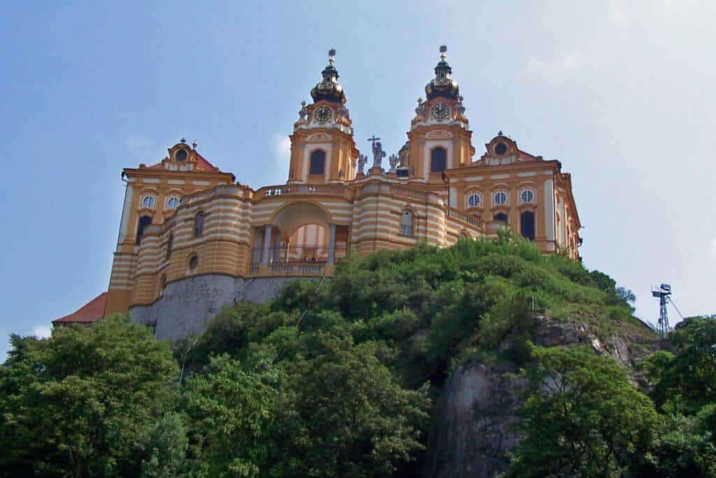 The majestic Melk Abbey perched on a rocky outcrop overlooking the Danube in Austria, its baroque architecture highlighted by ornate towers and a golden facade under a clear sky.