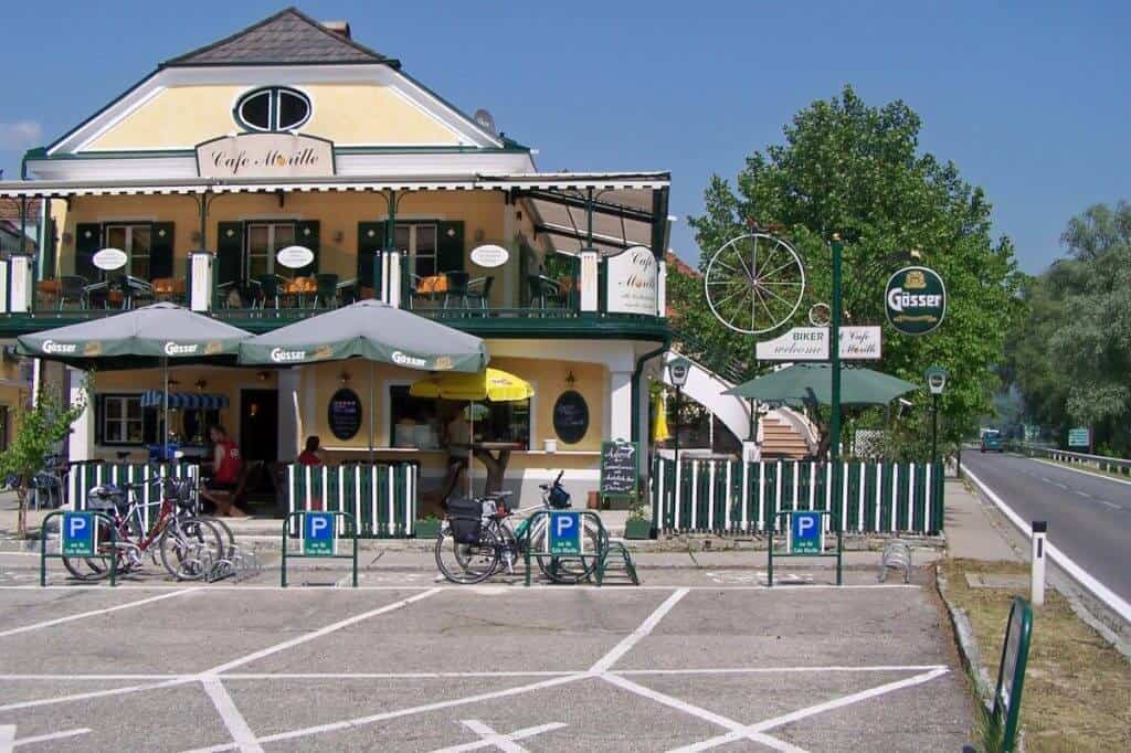 A welcoming café along the Danube Cycling Route in the Wachau region, with outdoor seating shaded by umbrellas, bicycles parked in front, and the iconic Gosser beer signs visible, suggesting a popular rest spot for cyclists.