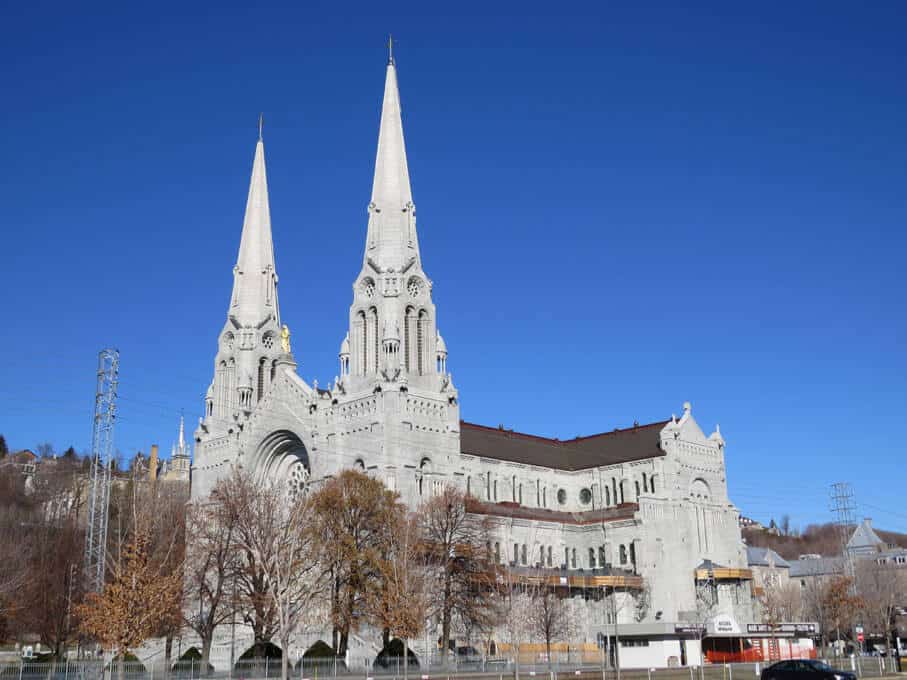 The Basilique de Sainte-Anne-de-Beaupré stands majestic against a clear blue sky near Quebec City. Its twin white spires and intricate stone façade are a testament to the grandeur of Gothic Revival architecture, serving as a beacon of faith and history in the region.