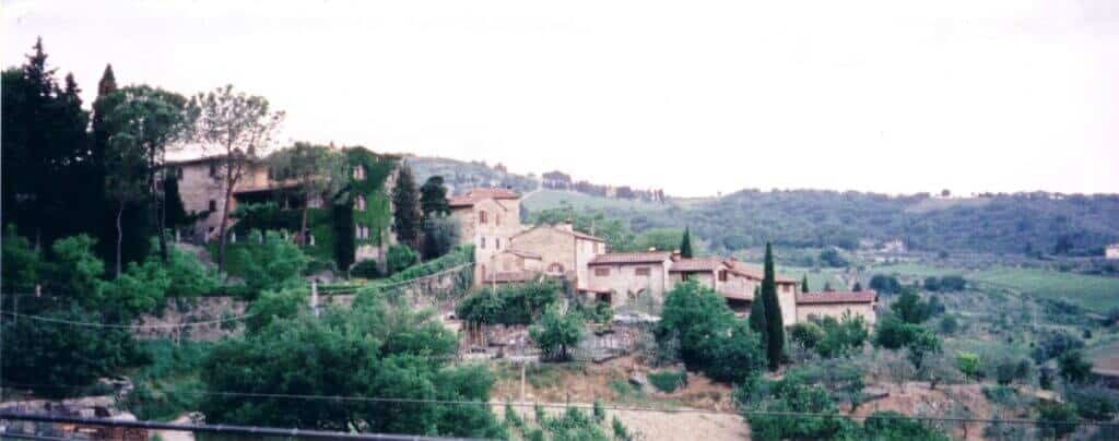 The small, historic village of Montefioralle in Tuscany nestles on a sloping hillside, with stone houses and cypress trees scattered across the landscape, epitomizing the rustic charm of the Italian countryside.